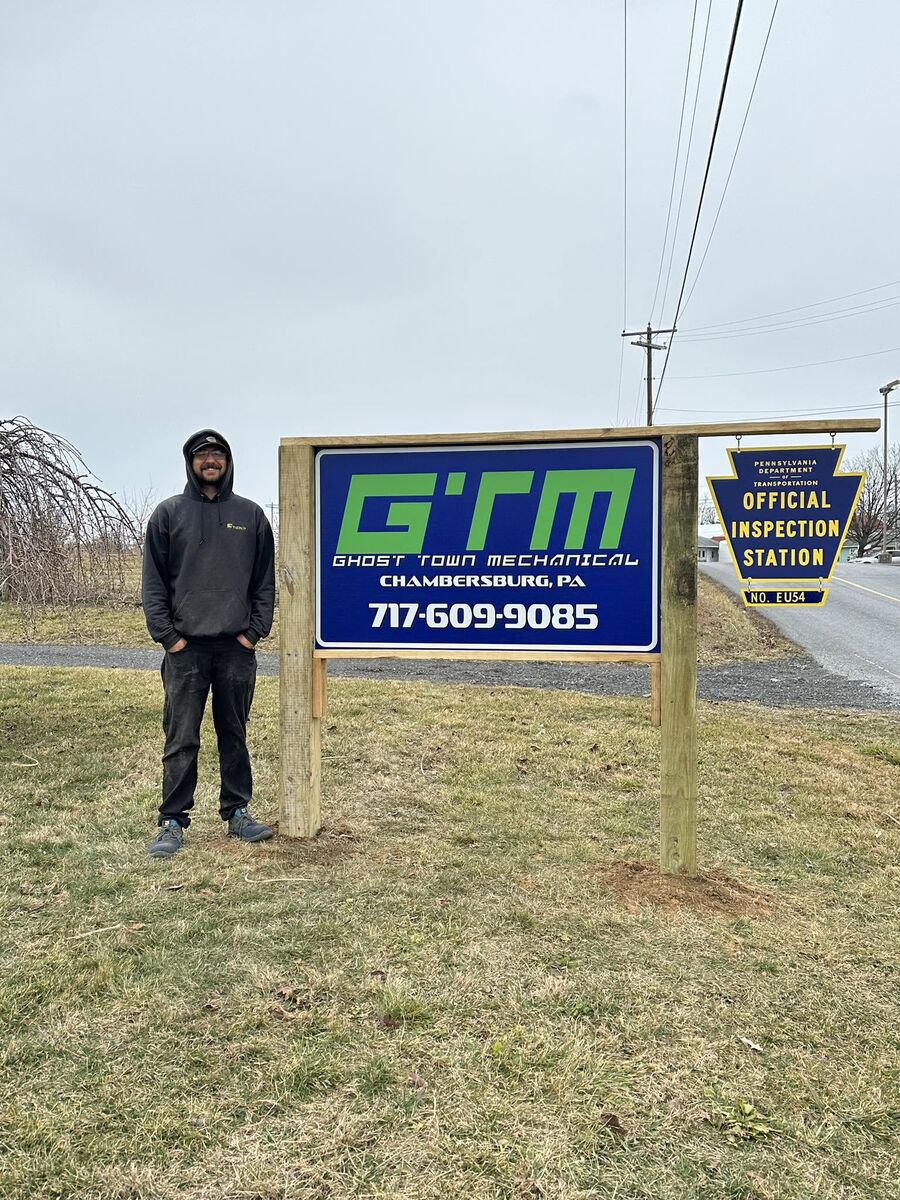 The owner of Ghost Town Mechanical standing next to the shop sign in Chambersburg